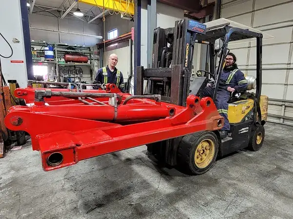 Red excavator boom moved on a forklift in the shop